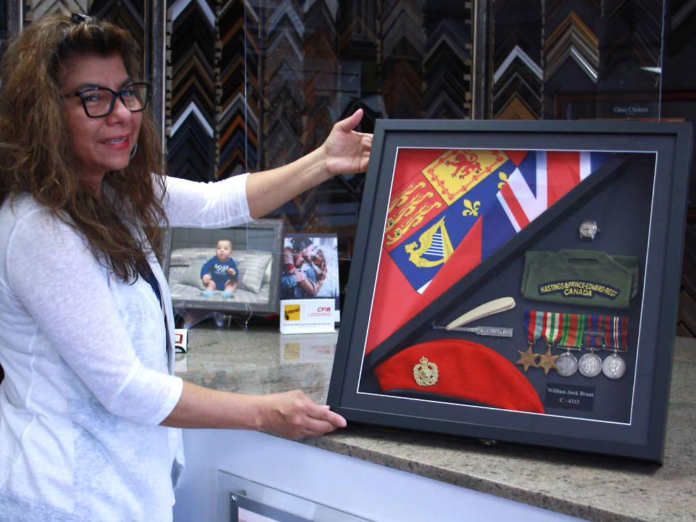 Frecia Correia, owner of Quinte Art & Custom Frame, holding military memorabilia framed in a custom shadow box